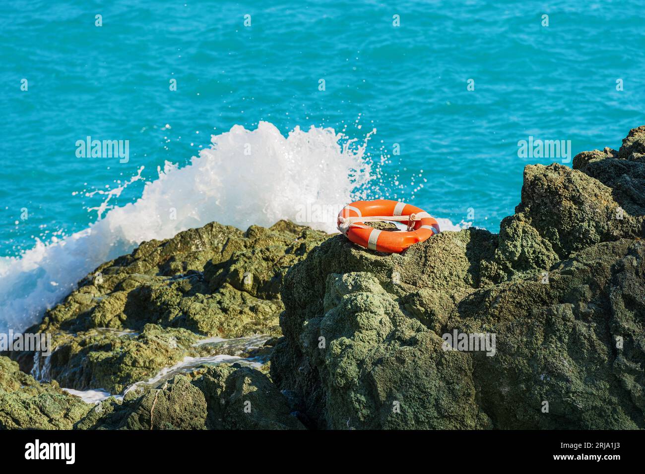 Orange life buoy (ring buoy) on a cliff with blue sea and white wave on background. Cinque Terre, La Spezia province, Italy, Europe. Stock Photo