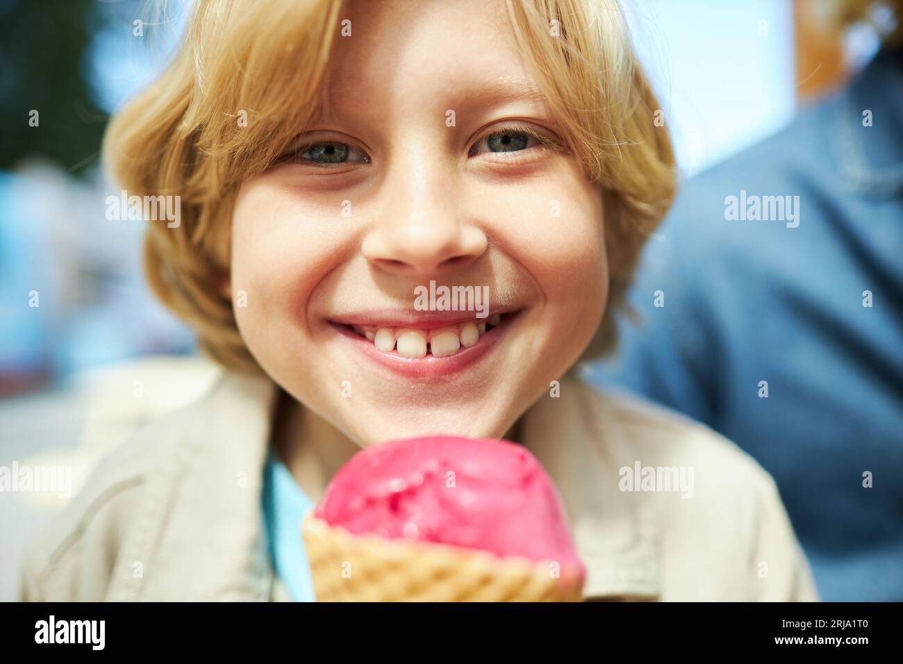Close up of happy boy eating ice cream cone outdoors at carnival and smiling at camera Stock Photo