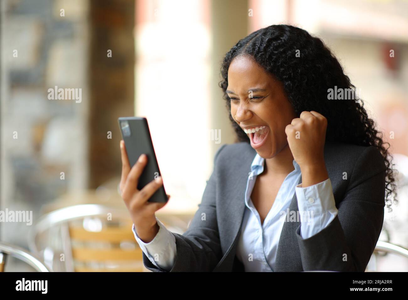 Excited black executive checking phone sitting in a bar terrace Stock Photo