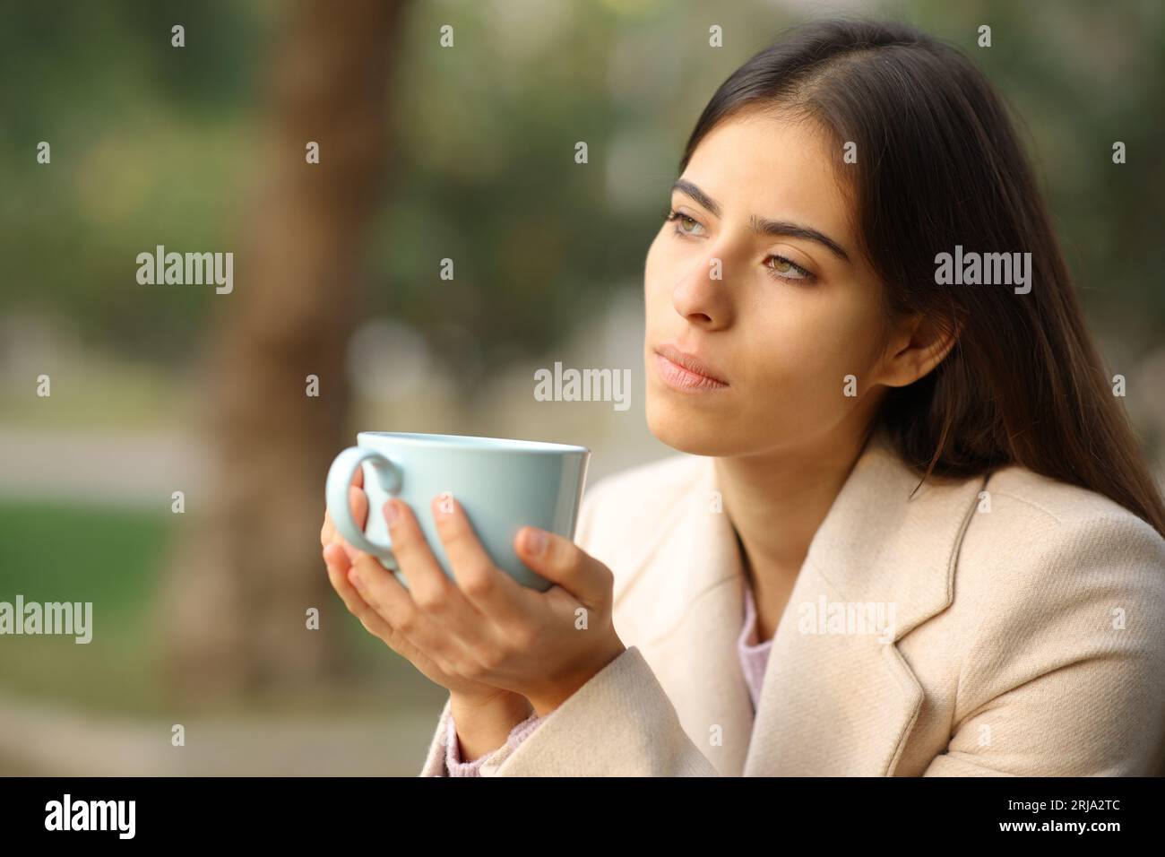 Pensive woman in winter holding coffee mug in a park Stock Photo