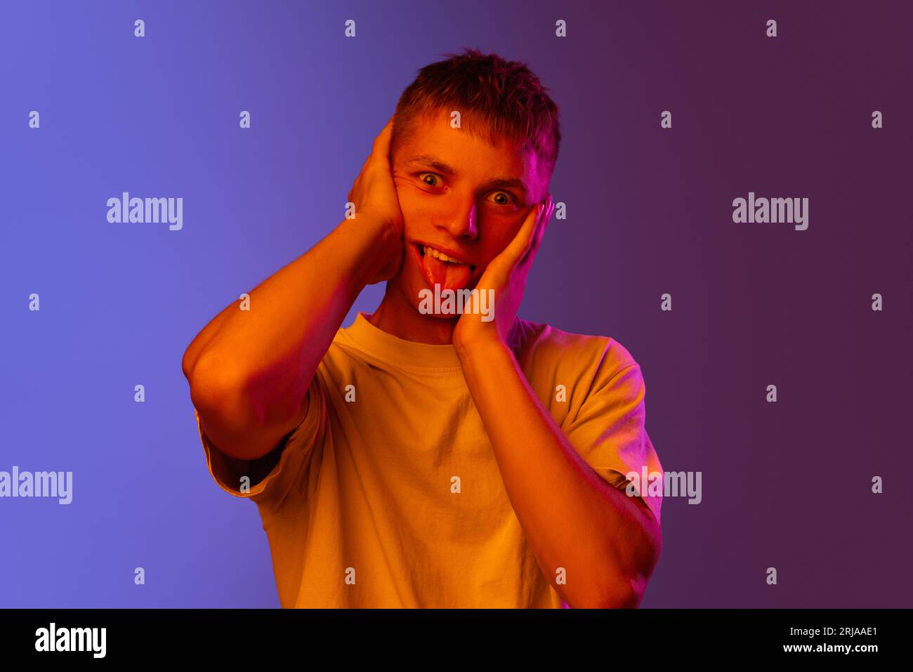 Young emotional guy posing with funny, meme, grimacing face against  gradient purple background in neon light Stock Photo - Alamy