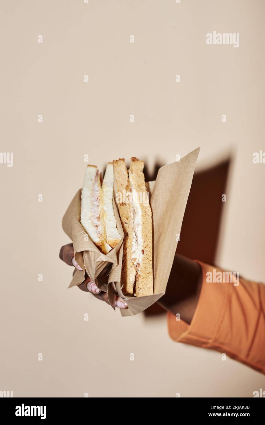 Vertical closeup of black woman holding sandwich in paper wrapping shot with flash Stock Photo