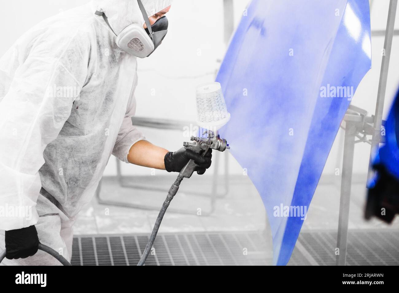 Man in protective mask and clothes sprays varnish to hood of car with a