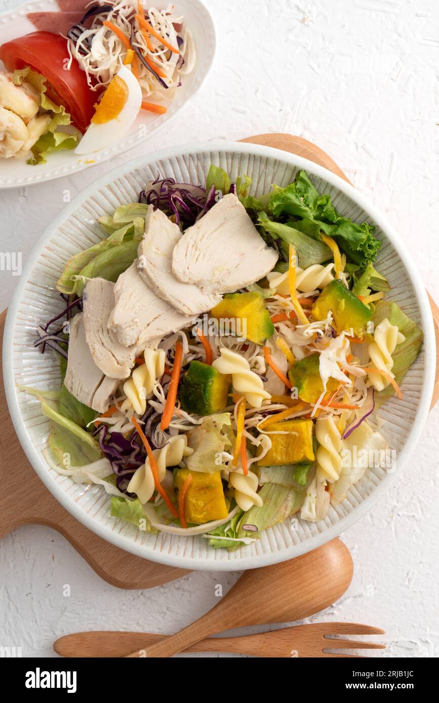 Fresh avocado lettuce salad bowl with sliced chicken meat and rotini in a plate on white table background. Stock Photo