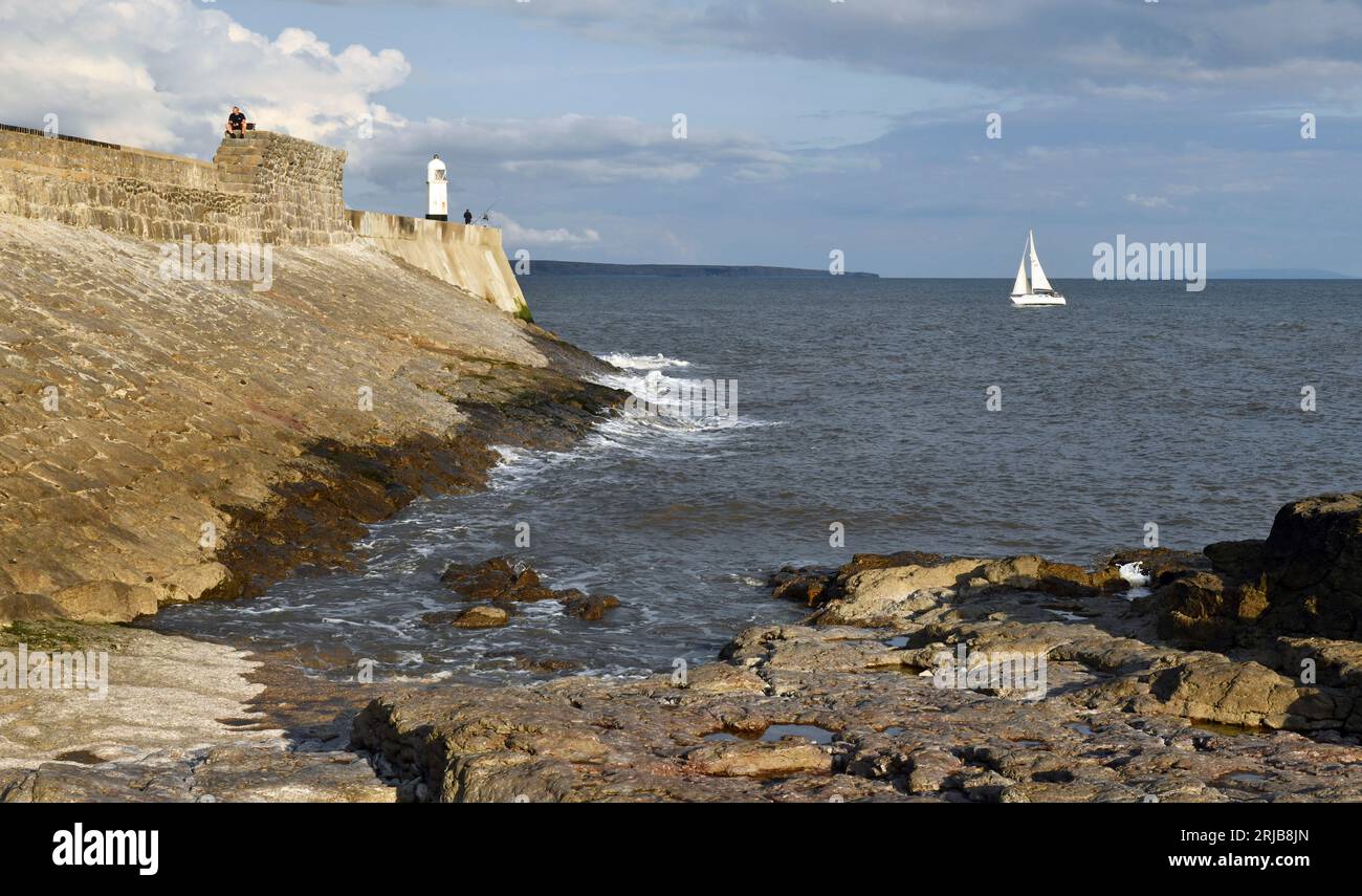Porthcawl Pier and the famous Lighthouse on a sunny summer evening in July from the beach coast rocks and feauturing a yacht heading into the harbour Stock Photo