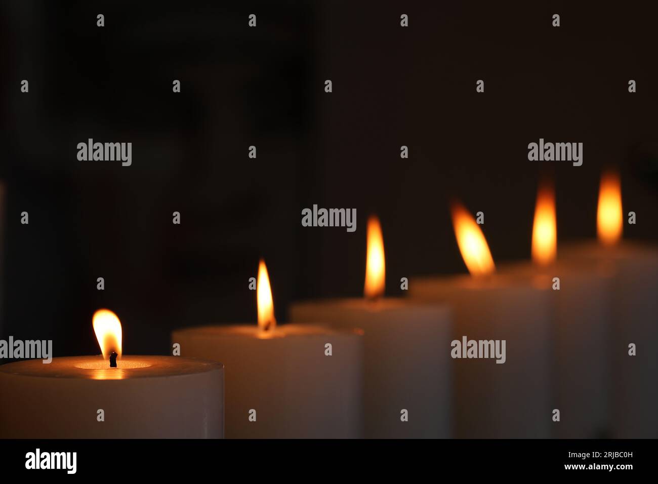 6 candles burning and flickering flame in against darkened background. Candle light vigil for remembering victims of crime or lost relatives. Stock Photo