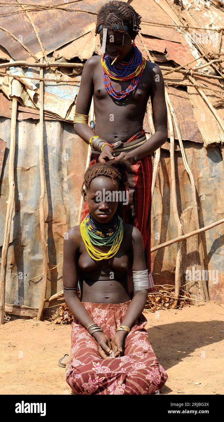 Daasanach girl combing a friend in front of his hut. Debub Omo Zone, Ethiopia. Stock Photo