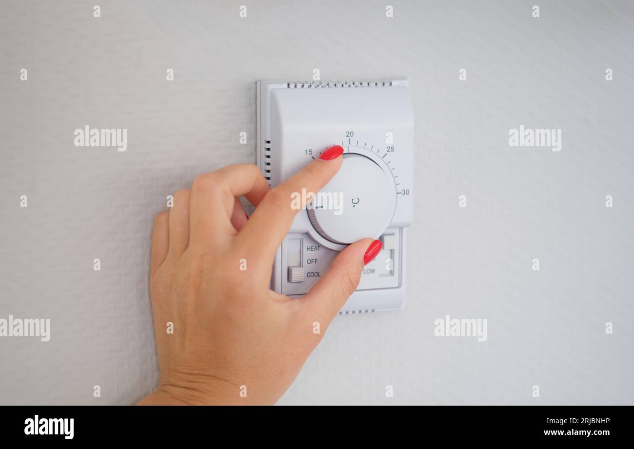 Woman hand adjusts or turns on wall temperature controller controller button Stock Photo