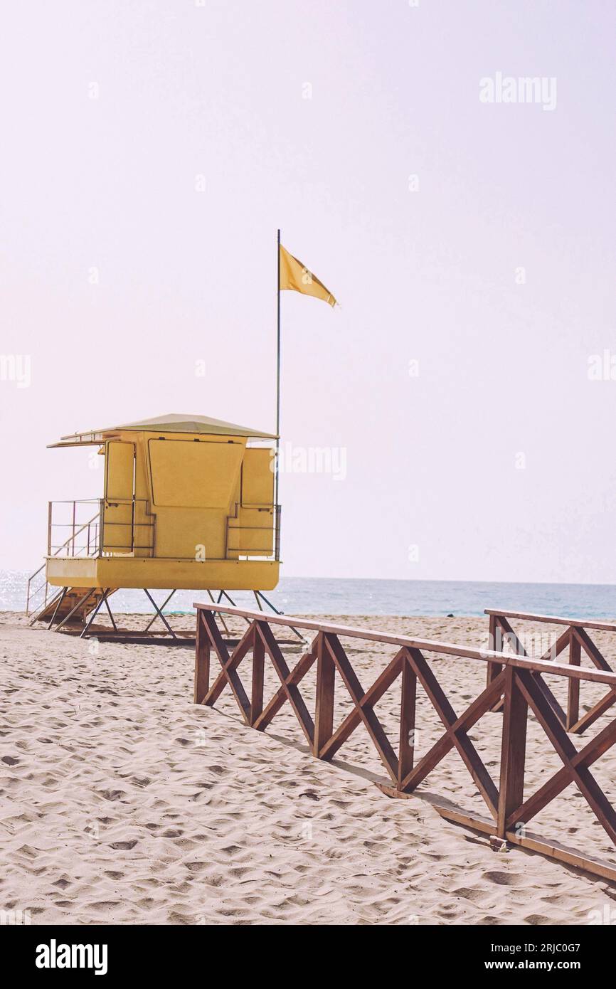Yellow lifeguard tower or station at a beach with a yellow flag.  All words and lettering removed from the structure Stock Photo