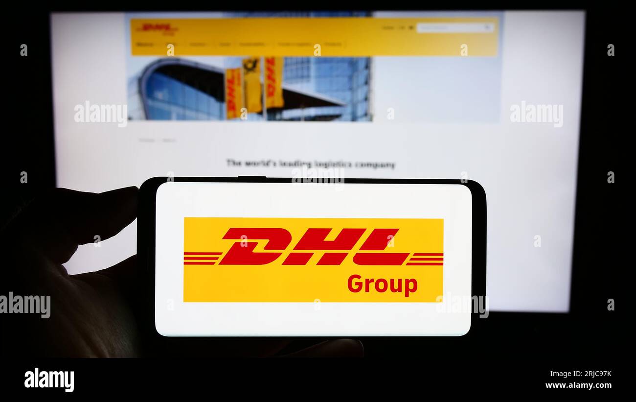 Person holding smartphone with logo of logistics company Deutsche Post AG (DHL Group) on screen in front of website. Focus on phone display. Stock Photo