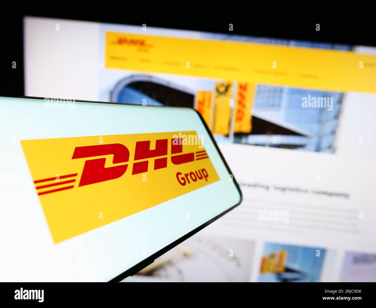 Smartphone with logo of logistics company Deutsche Post AG (DHL Group) on screen in front of website. Focus on center-left of phone display. Stock Photo