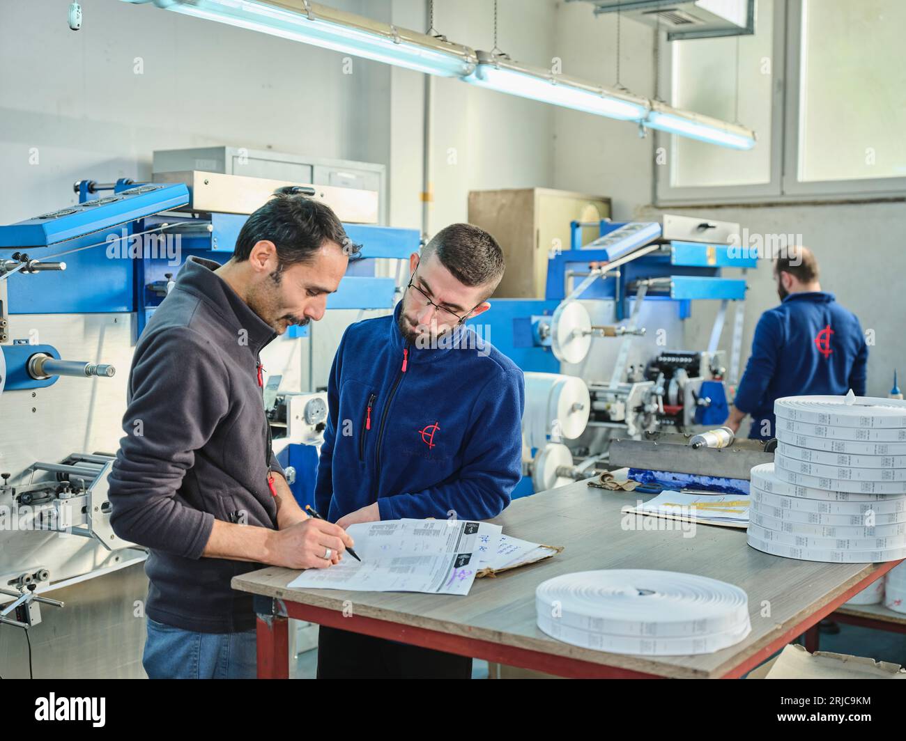 people working in a sticker printing factory. worker uses a stickier ...