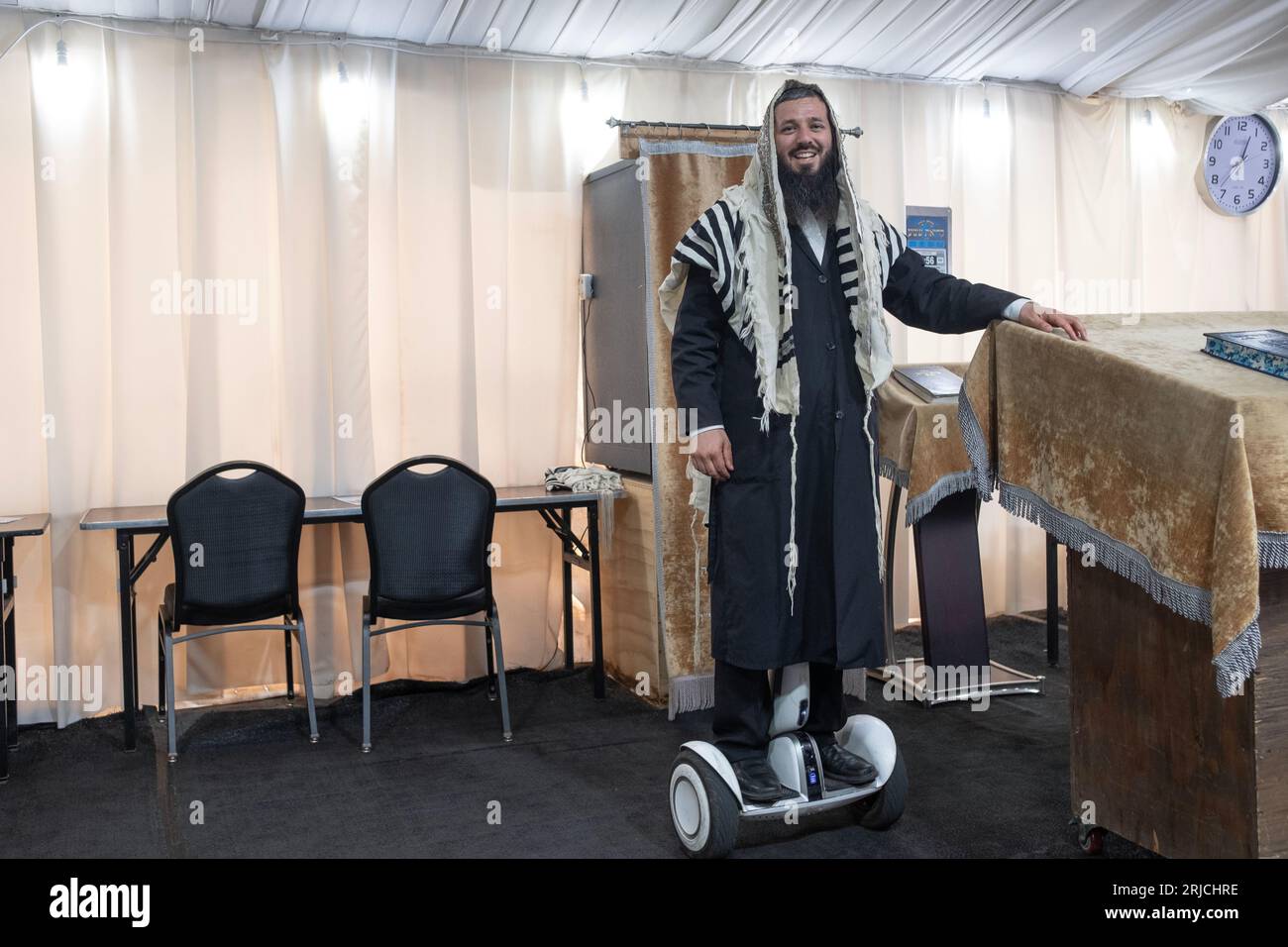 A sexton - shammash - at a synagogue with a few tents. His hoverboard lets him be everywhere at once. In Mosey, New York. Stock Photo