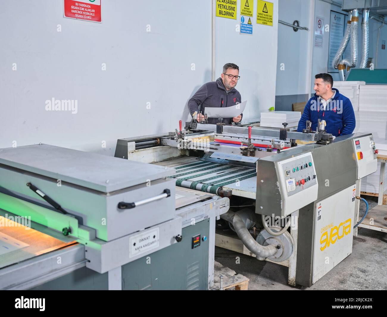 people working in a sticker printing factory. worker uses a stickier ...