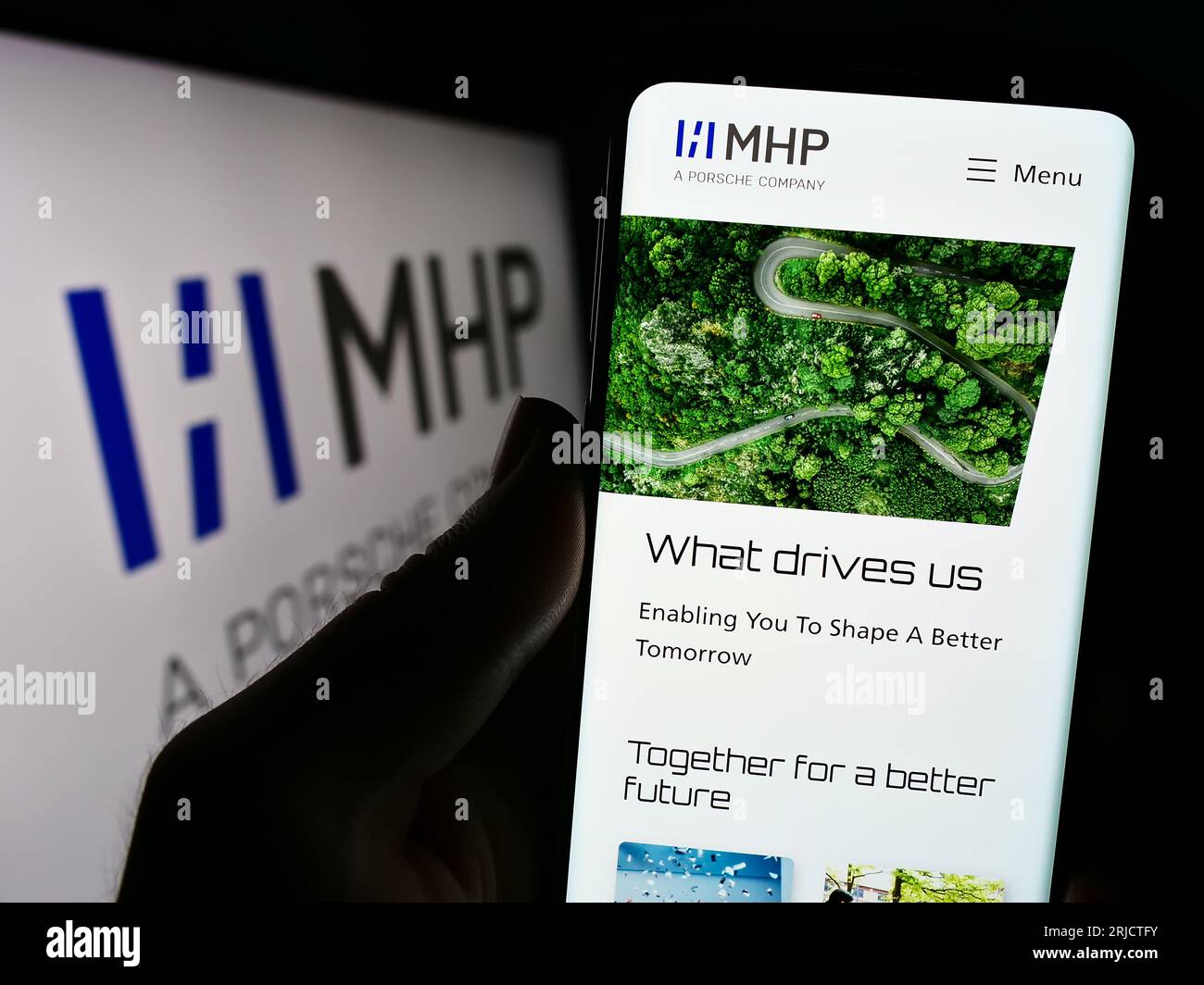 Person holding mobile phone with website of company MHP Management- und IT-Beratung GmbH on screen with logo. Focus on center of phone display. Stock Photo