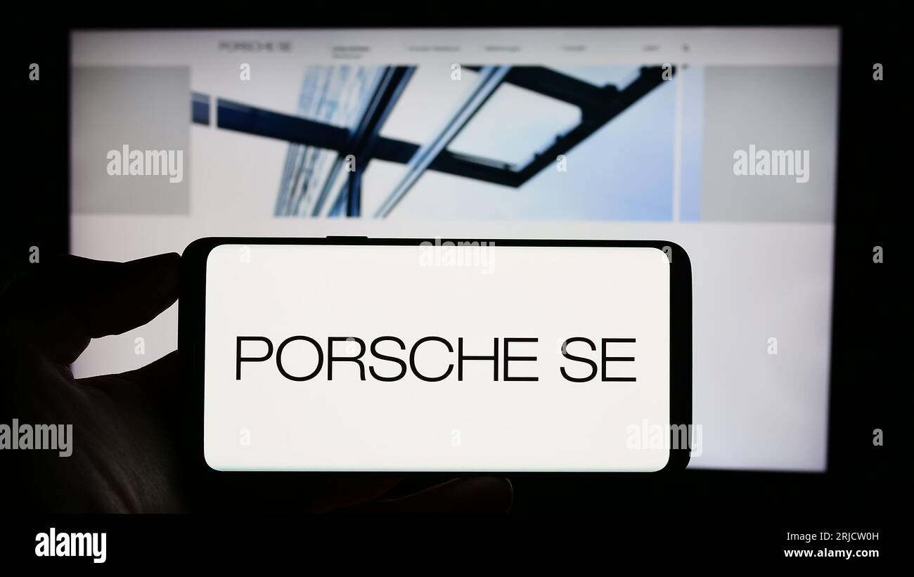 Person holding cellphone with logo of German company Porsche Automobil Holding SE on screen in front of business webpage. Focus on phone display. Stock Photo