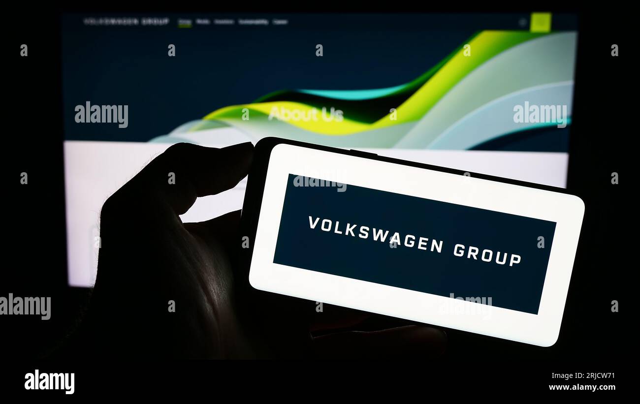Person holding smartphone with logo of German automotive company Volkswagen AG on screen in front of website. Focus on phone display. Stock Photo