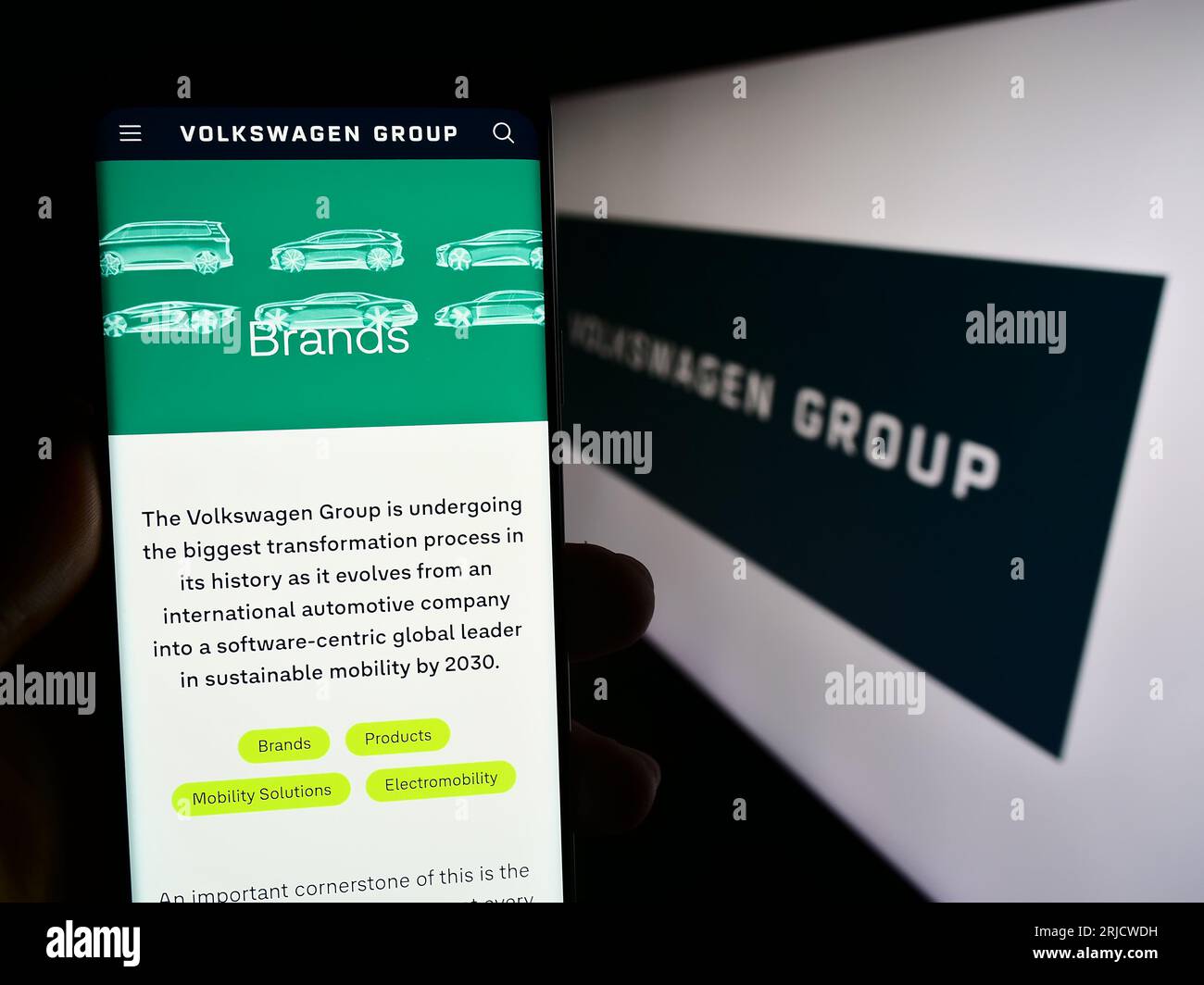Person holding smartphone with webpage of German automotive company Volkswagen AG on screen in front of logo. Focus on center of phone display. Stock Photo