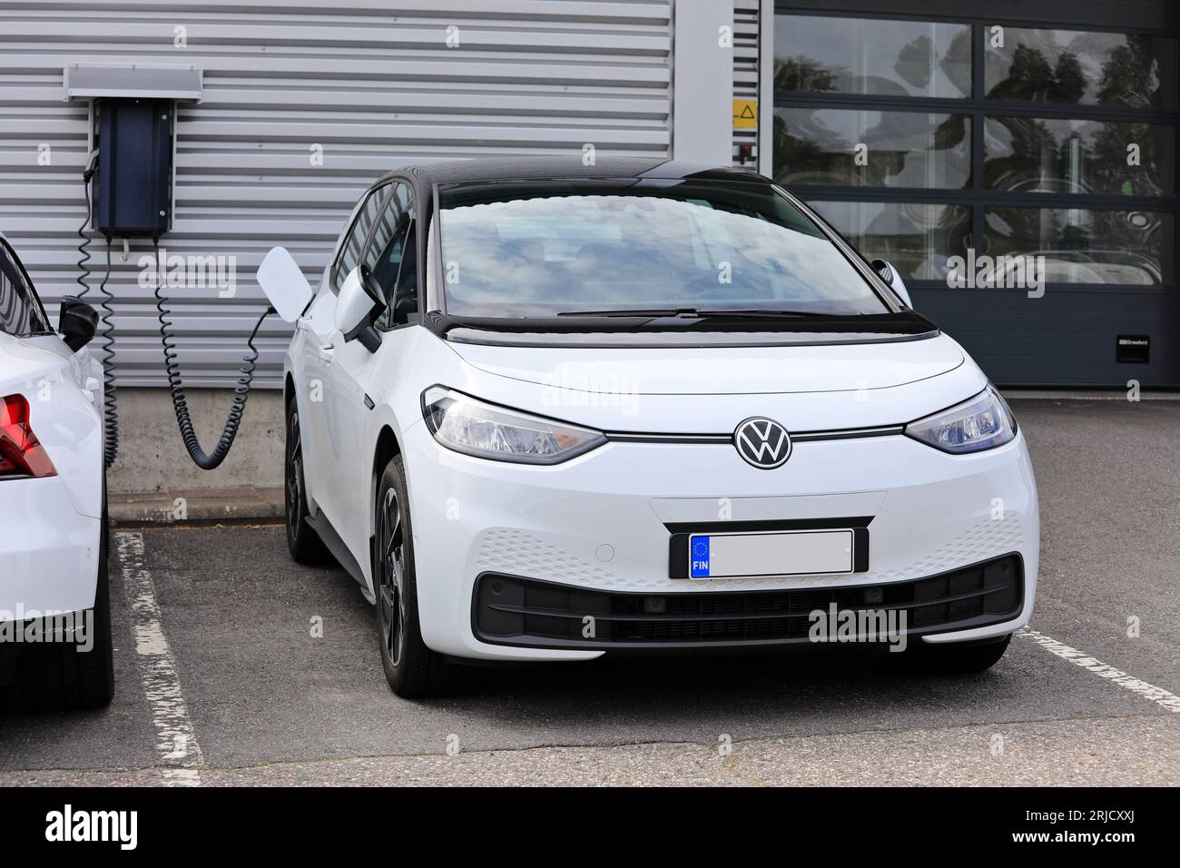 White Volkswagen VW ID.3 1st model charging battery at a wall charger of a car dealership. Salo, Finland. August 13, 2023. Stock Photo