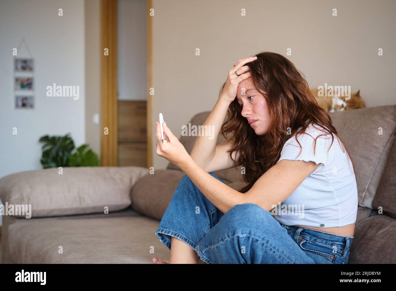Sick woman holding thermometer sitting on the sofa Stock Photo