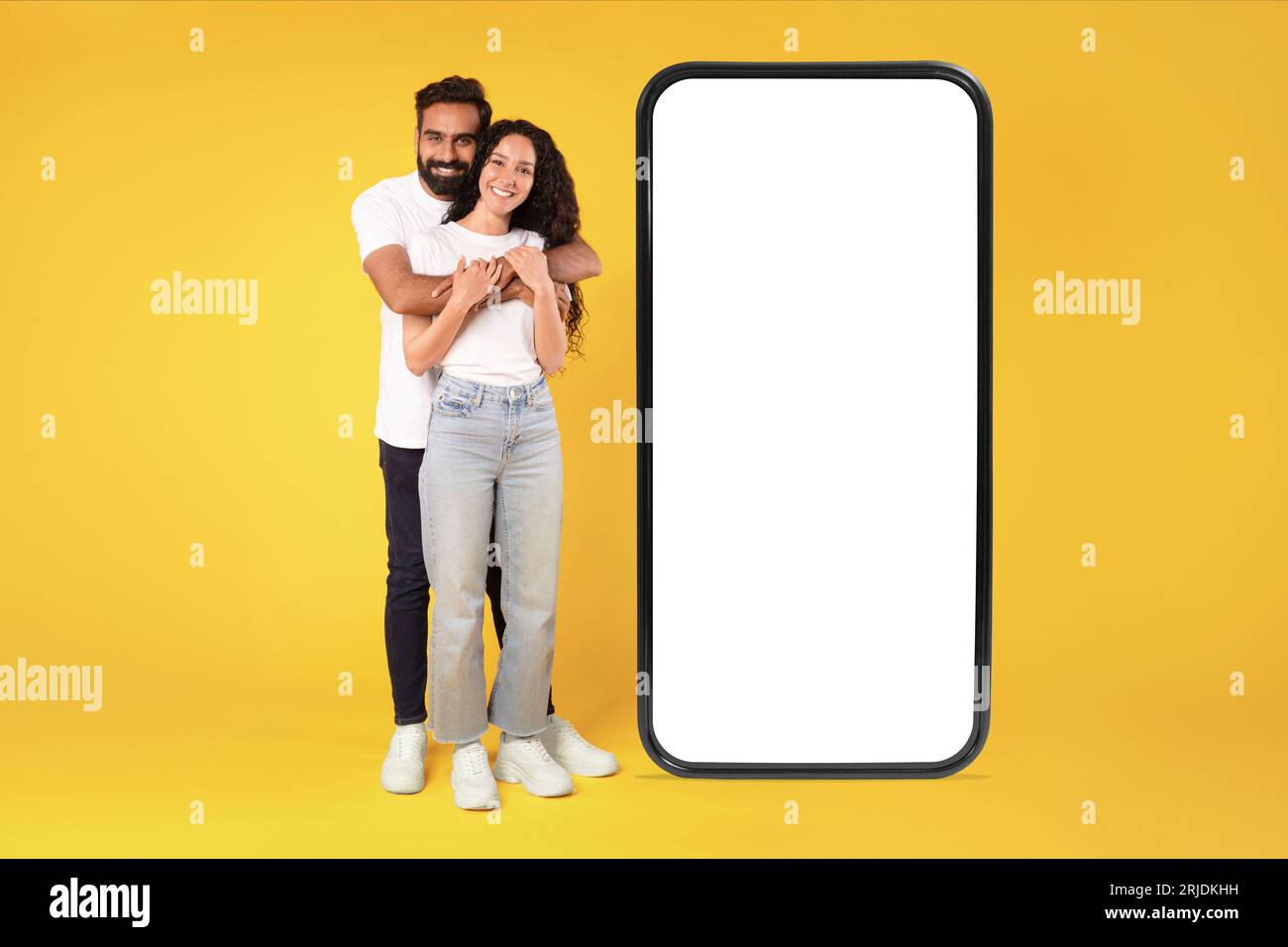 Arab couple hugging near big smartphone screen over yellow background ...