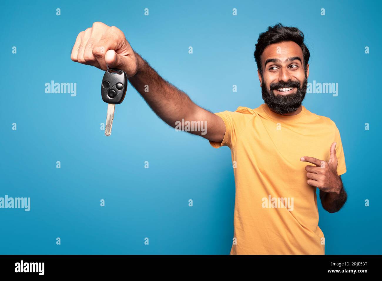 Excited indian man driver holding in hand new car key, pointing at it and smiling isolated on blue background Stock Photo