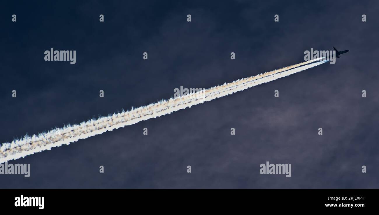 Transport airplane makes the very strong trace line of chemtrails on blue sky. Conspiracy theory. Stock Photo