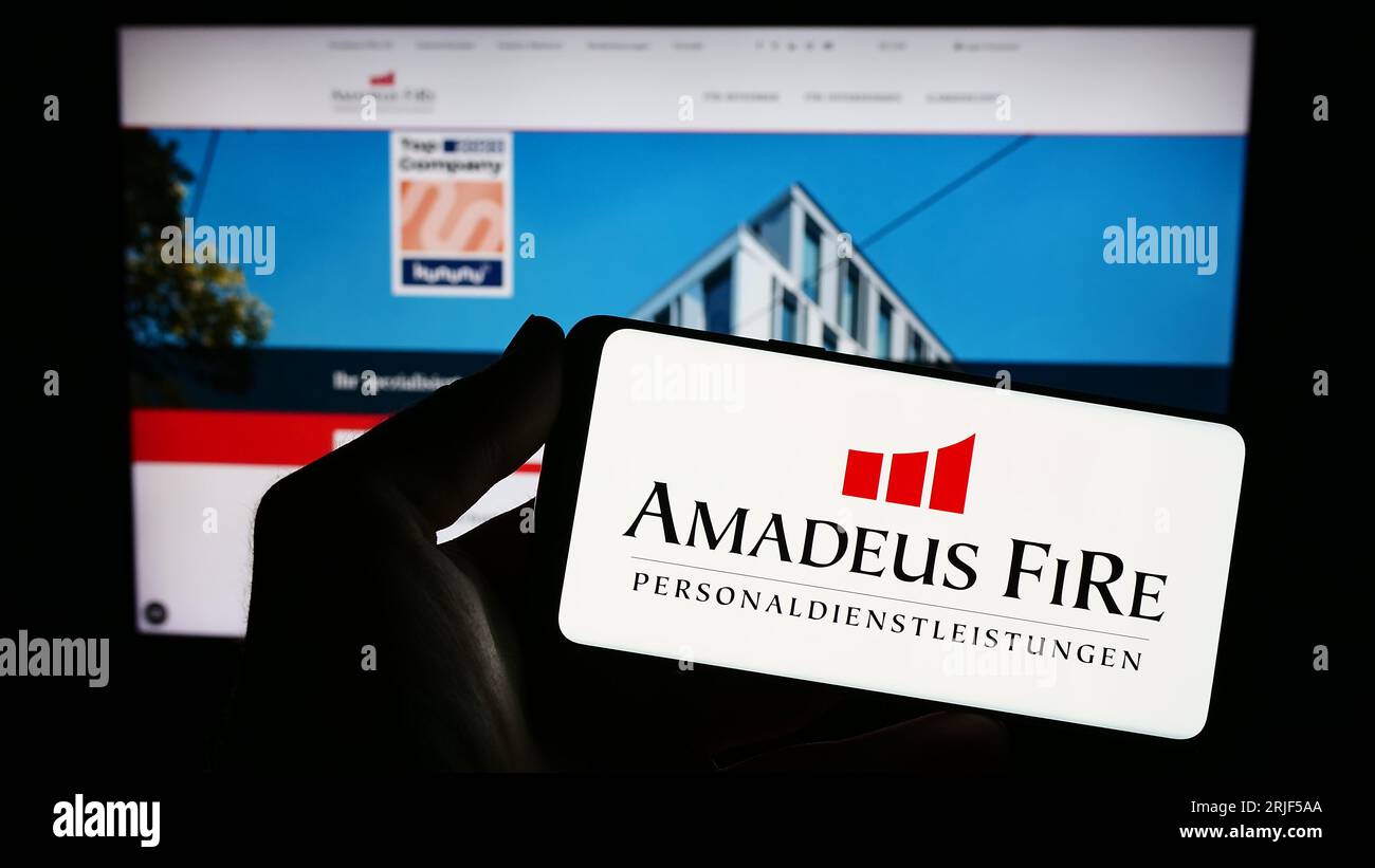 Person holding smartphone with logo of German recruitment company Amadeus FiRe AG on screen in front of website. Focus on phone display. Stock Photo