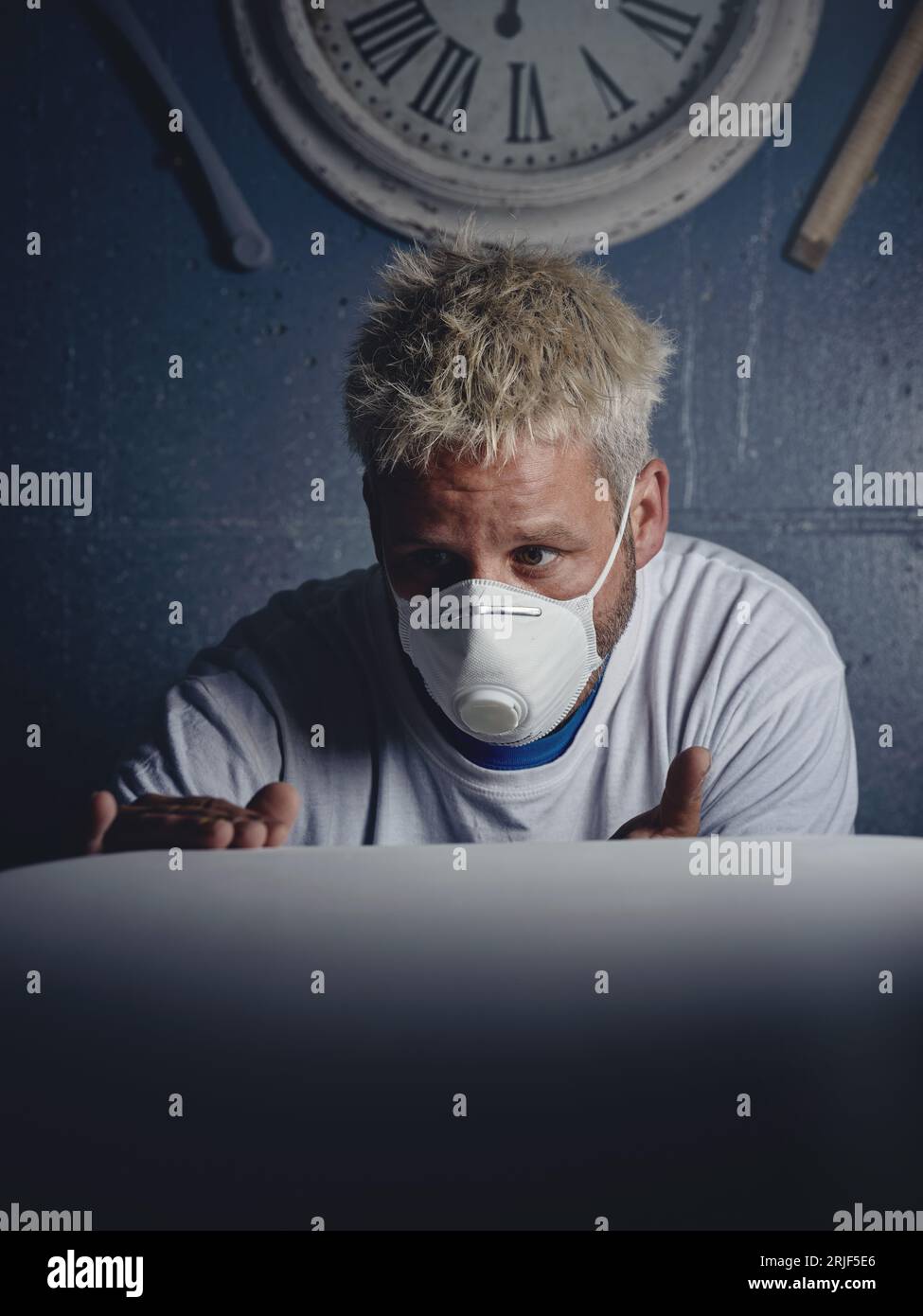 Serious concentrated blond haired male master making and checking white surfboard while observing and touching it in workshop Stock Photo