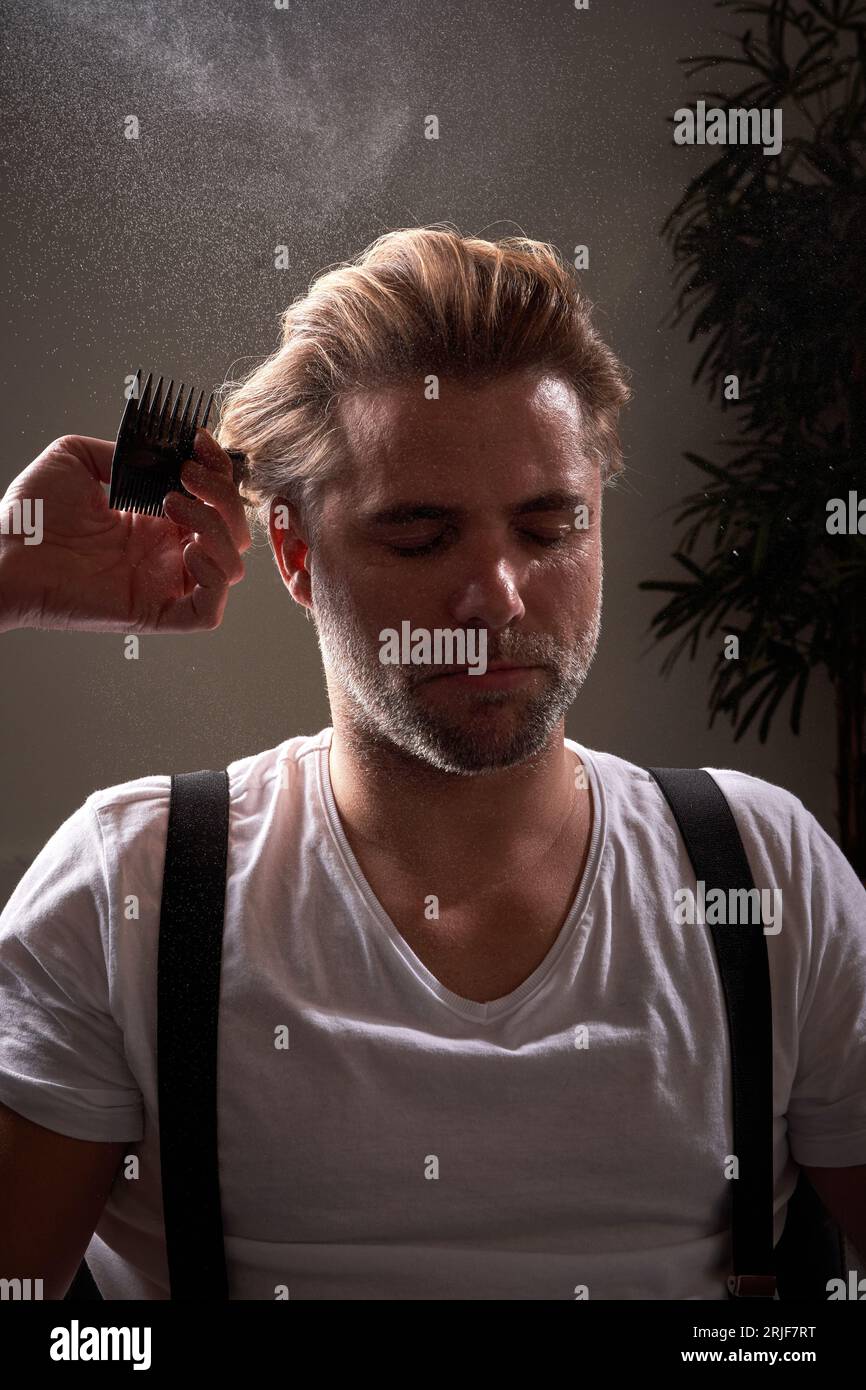 Crop professional barber styling hair of unshaven male client with eyes closed in barbershop Stock Photo