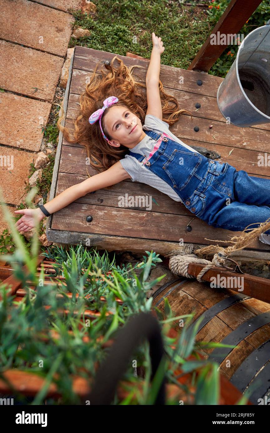 content-preteen-girl-in-denim-overall-looking-up-with-dreamy-face-while