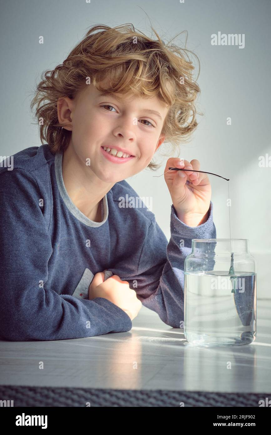 Positive little kid with curly blond hair putting toy small fishing rod  into transparent glass jar of water while looking at camera against white  back Stock Photo - Alamy