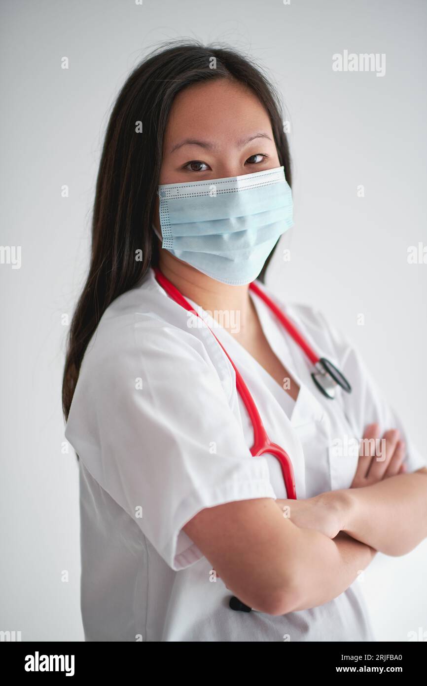 Side view of confident woman in medical uniform with stethoscope crossing arms and looking at camera on white background Stock Photo