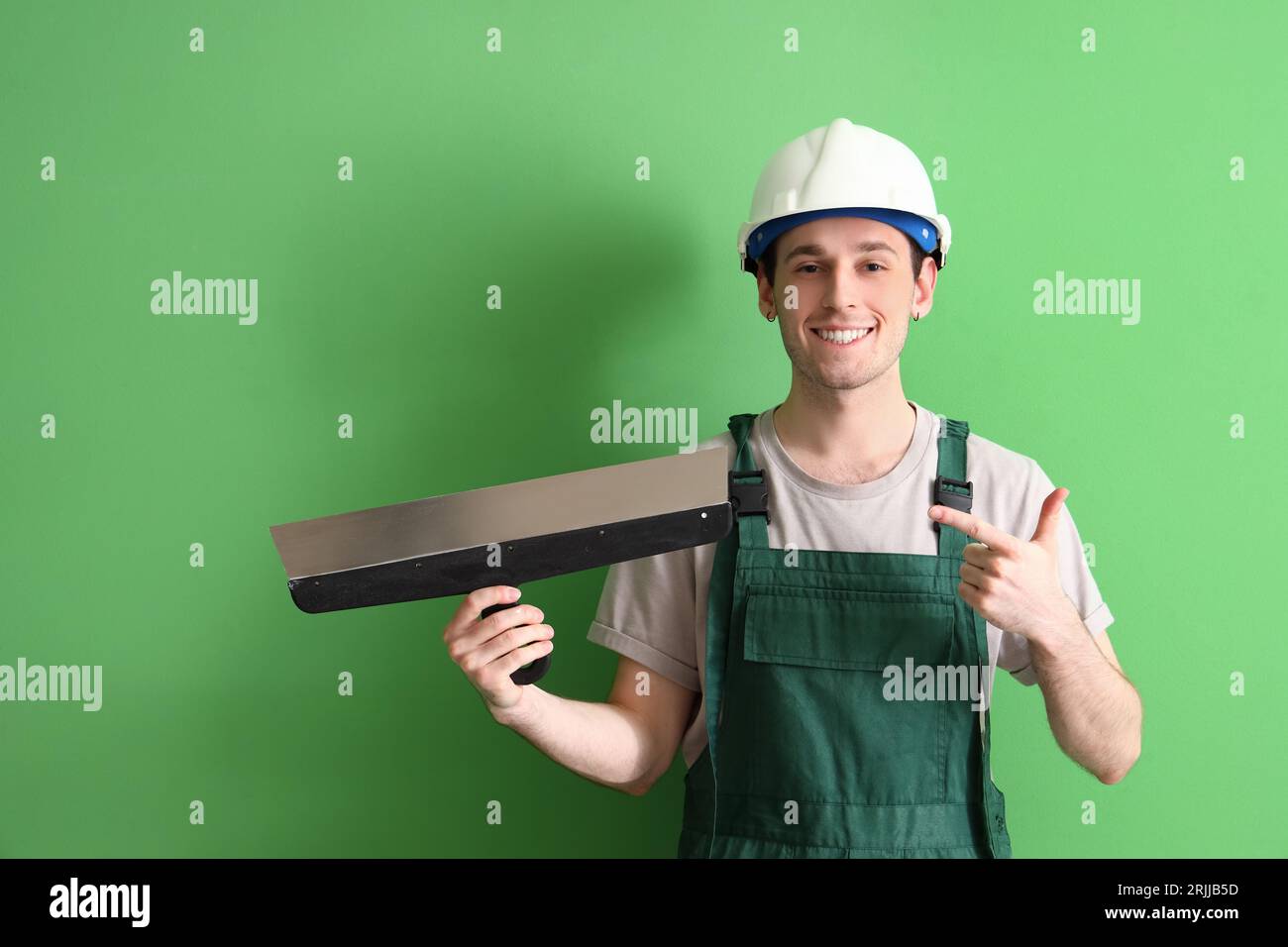 Male worker pointing at putty knife on green background Stock Photo - Alamy