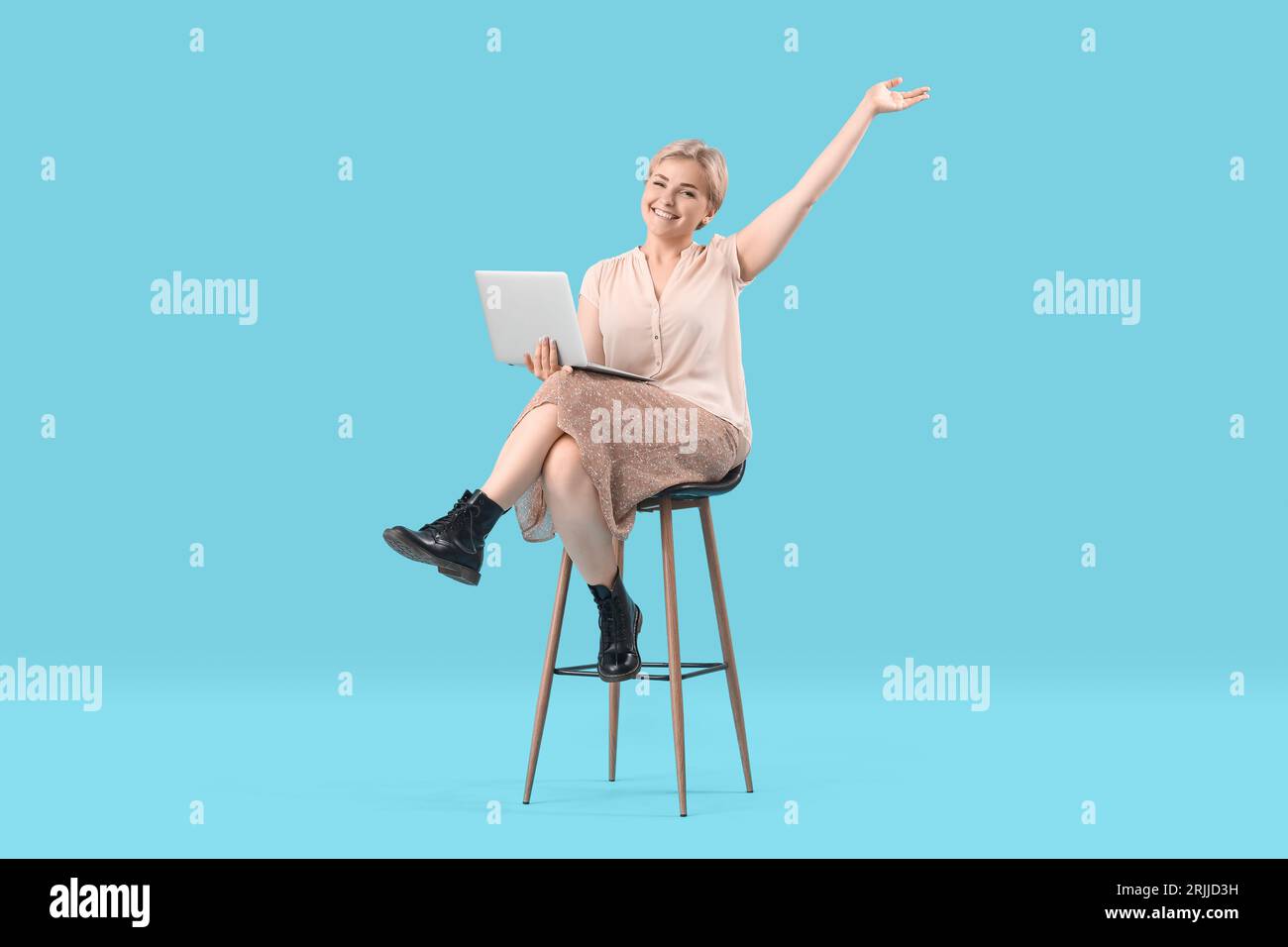 Happy young female programmer with laptop sitting on chair against blue ...