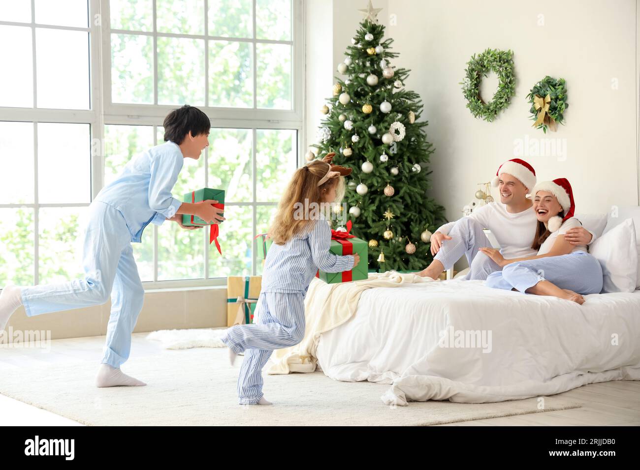 Little children with Christmas presents running to their parents in bedroom Stock Photo