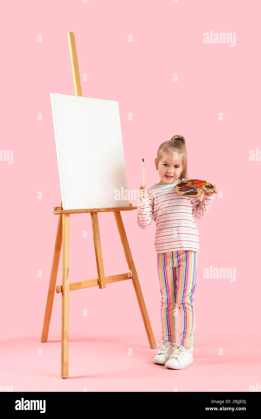 Cute little girl with paint palette, brush and easel on pink background ...