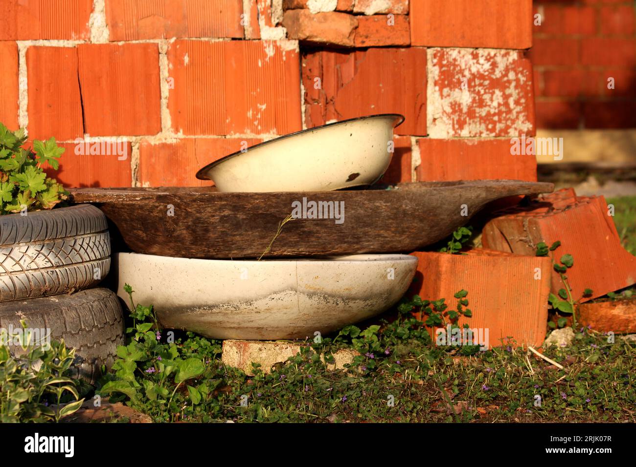 Bunch of old junk in suburban family house backyard next to red building blocks wall consisting of old white partially rusted metallic washbowl on top Stock Photo