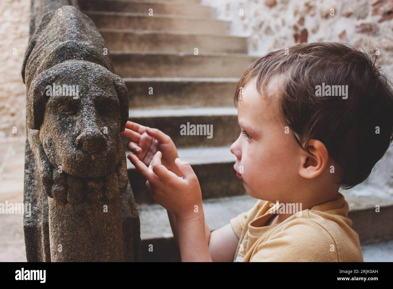 Kid and medieval stone dog. Boy is looking at the decoration of old outdoor staircase, selective focus. Meeting of the past and future. Stock Photo