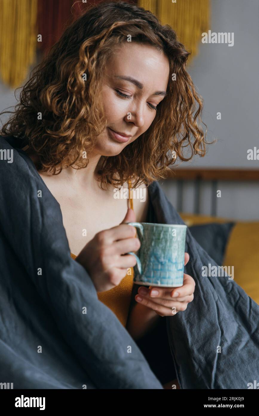 Young girl in bed with a mug of hot drink. Relaxing cannabis drink
