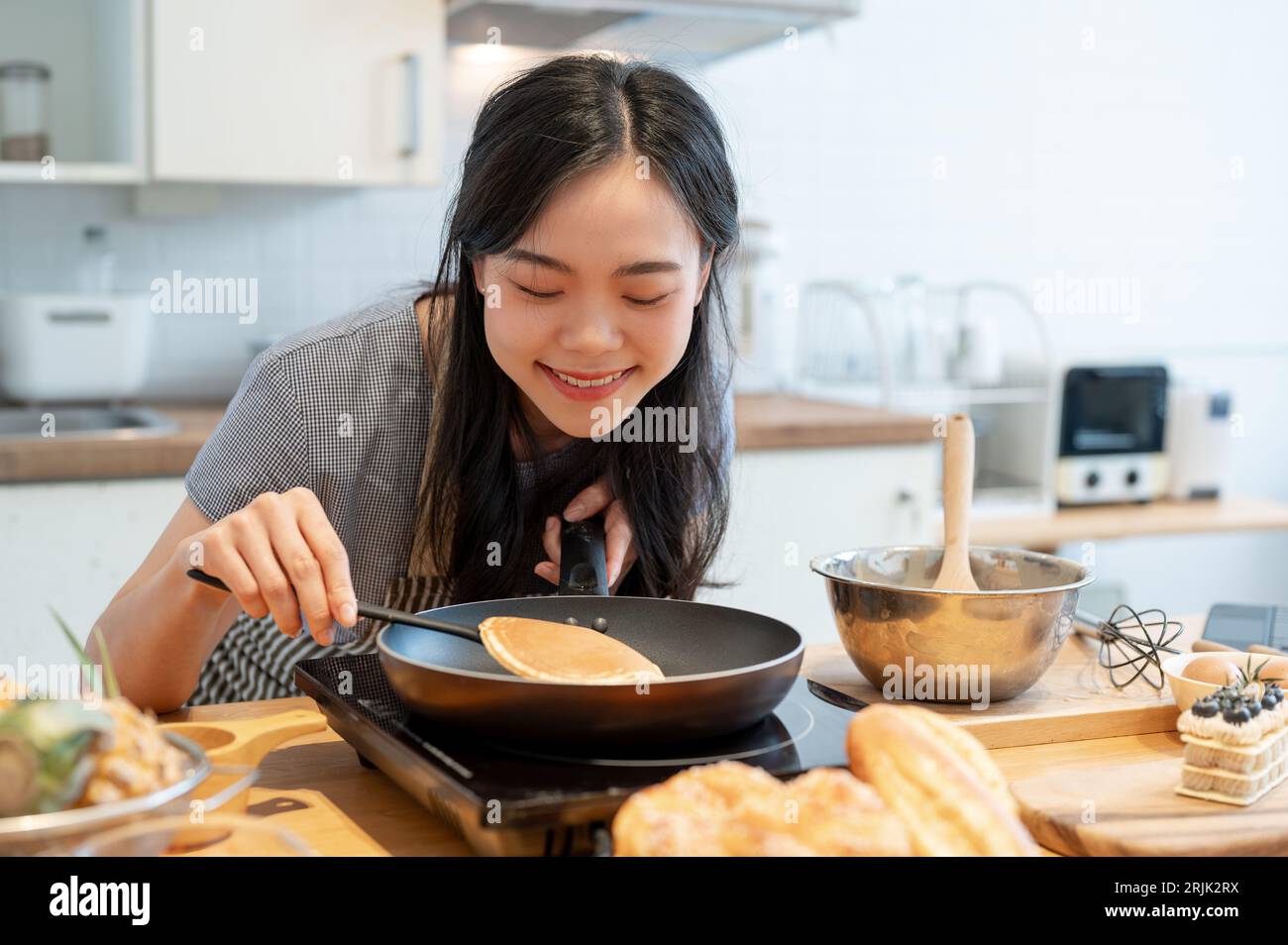 https://c8.alamy.com/comp/2RJK2RX/a-happy-and-lovely-young-asian-woman-flipping-a-pancake-in-a-pan-with-a-spatula-enjoys-cooking-pancakes-in-the-kitchen-preparing-homemade-breakfast-2RJK2RX.jpg