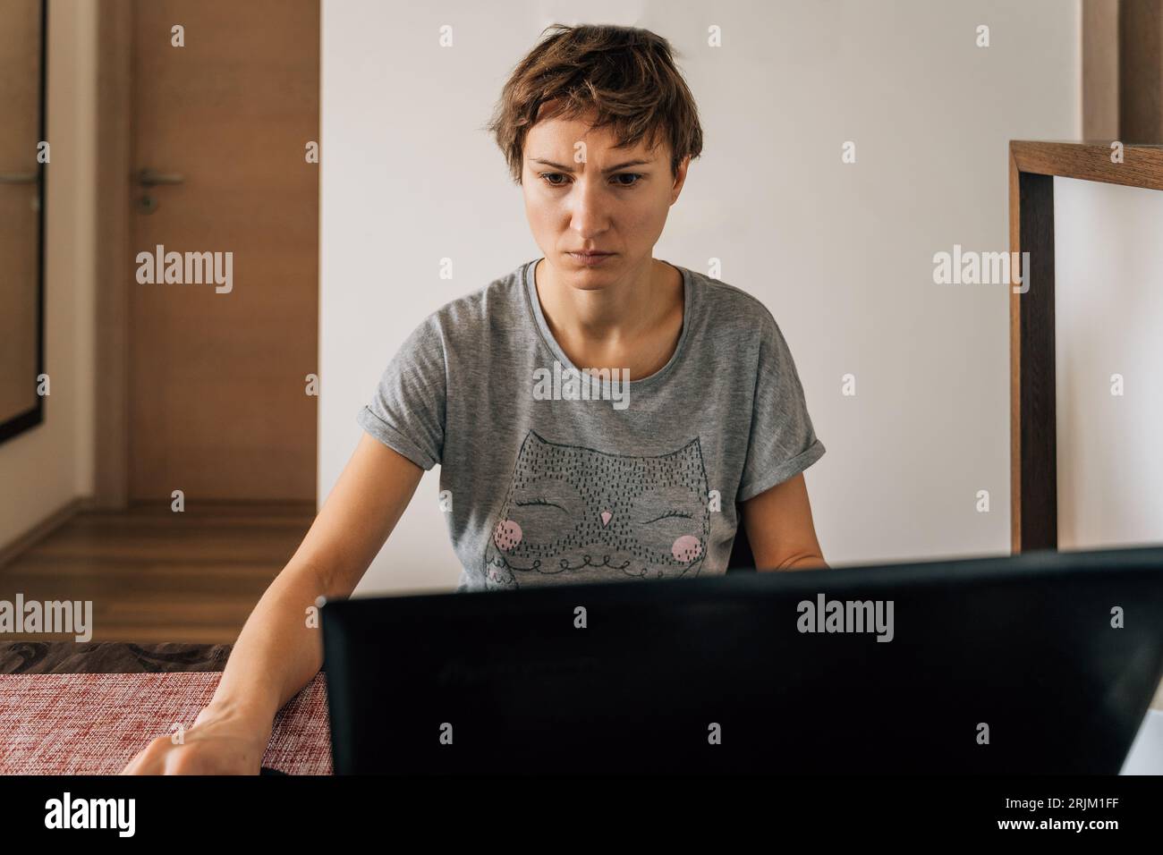 A woman in home clothes works at home at laptops with a tense look. Stock Photo