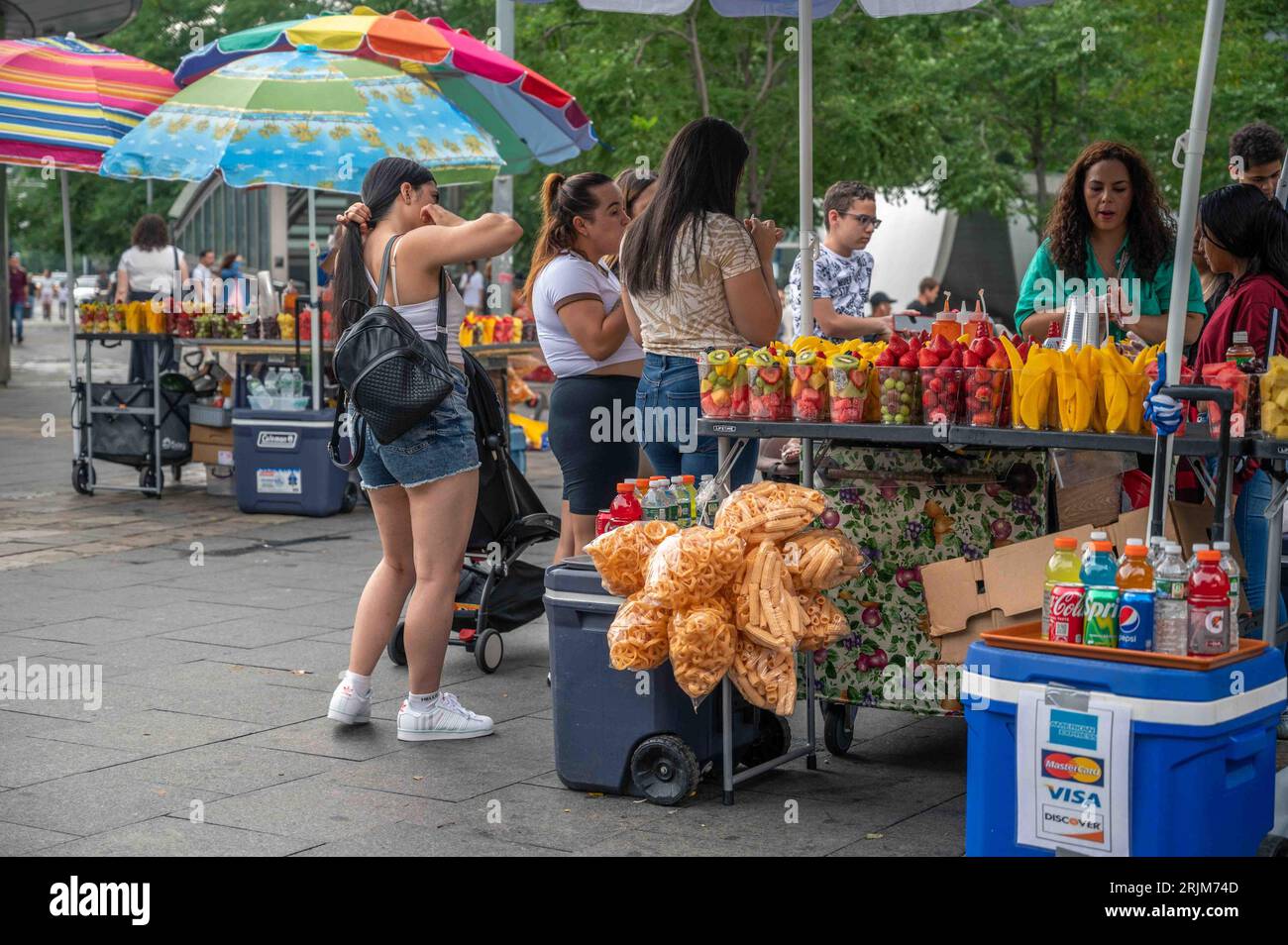 New York, NY 07182023 Fresh fruit stand with colorful umbrellas, customers, and rows of