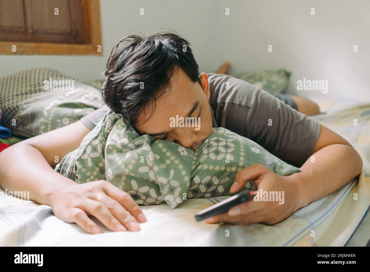 Portrait of Asian man fall asleep while holding smartphone laying down