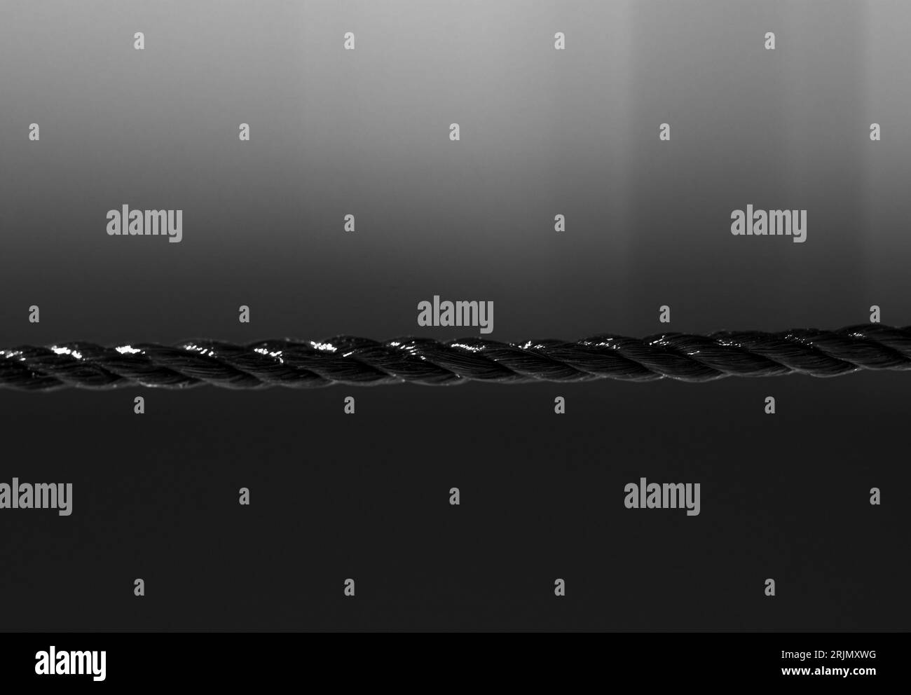 Black nylon rope in horizontal direction. Isolated on blurred black background. Close-up. Copy space. Stock Photo