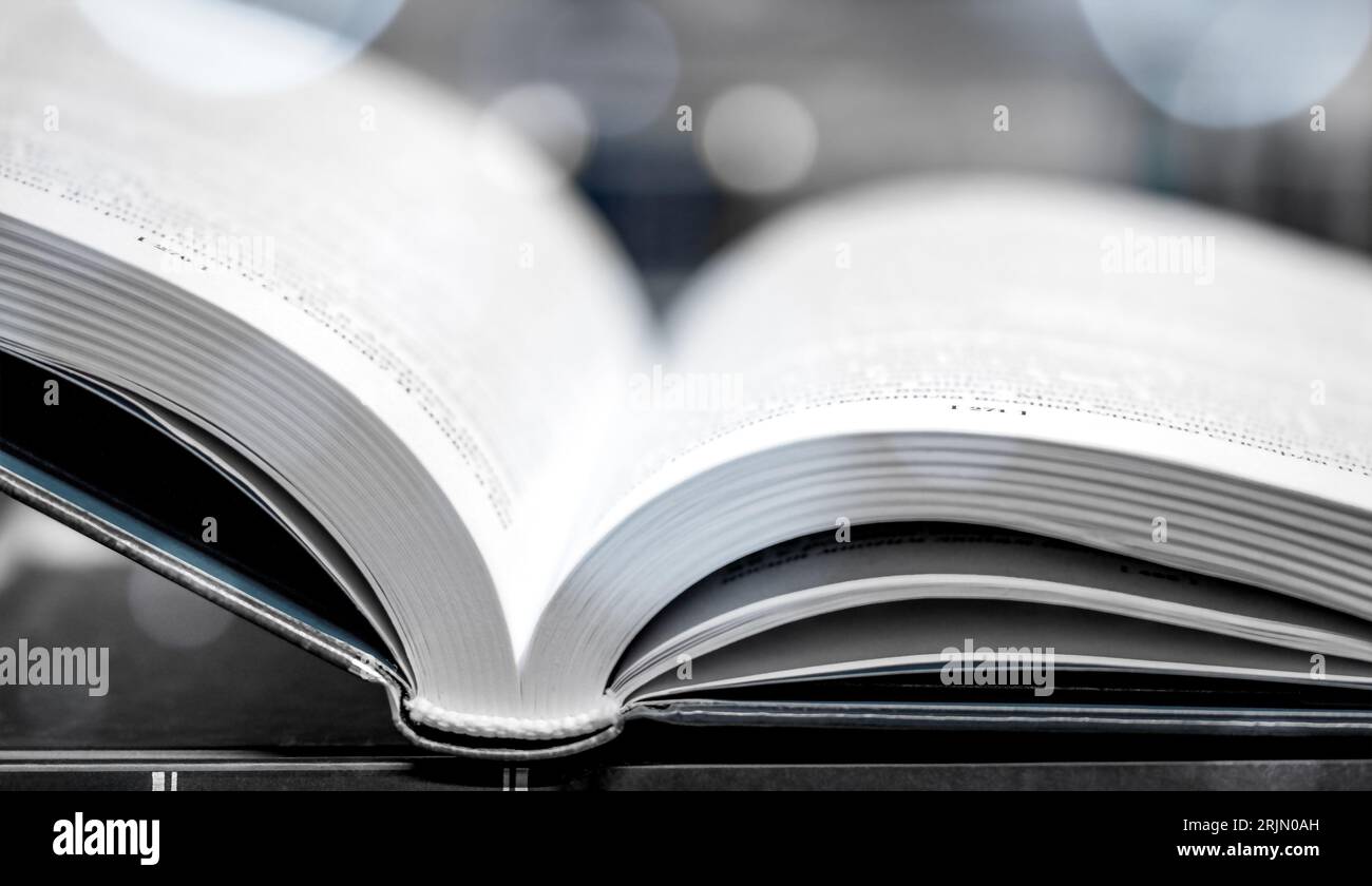 Open illuminated book on wooden table with glitters. Book lying open on desk in library. Glowing pages. Stock Photo