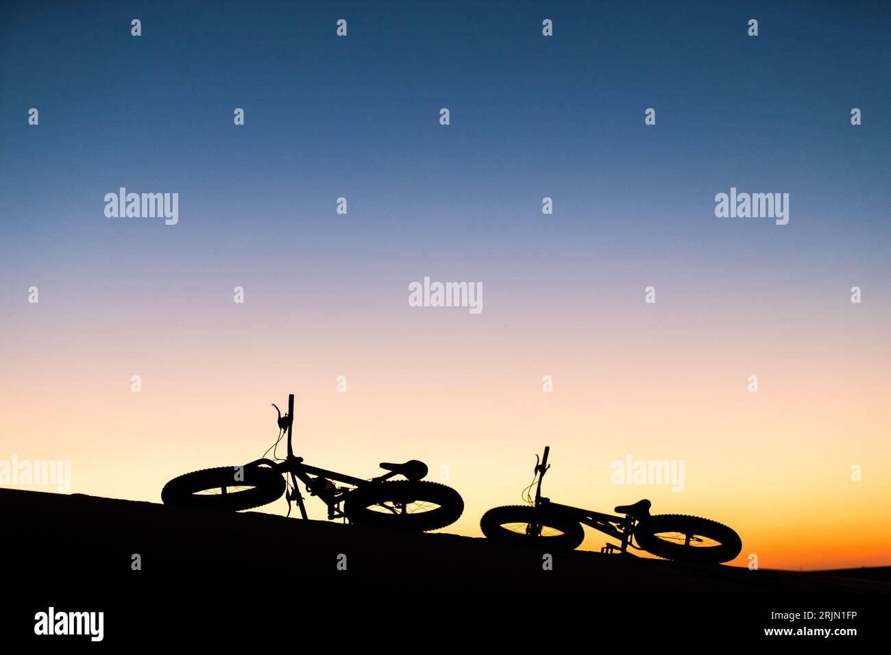 Sunset silhouette of two Fat bikes fat bicycles Namibia Swakopmund sand dunes adventure tourism Africa fun activities Stock Photo