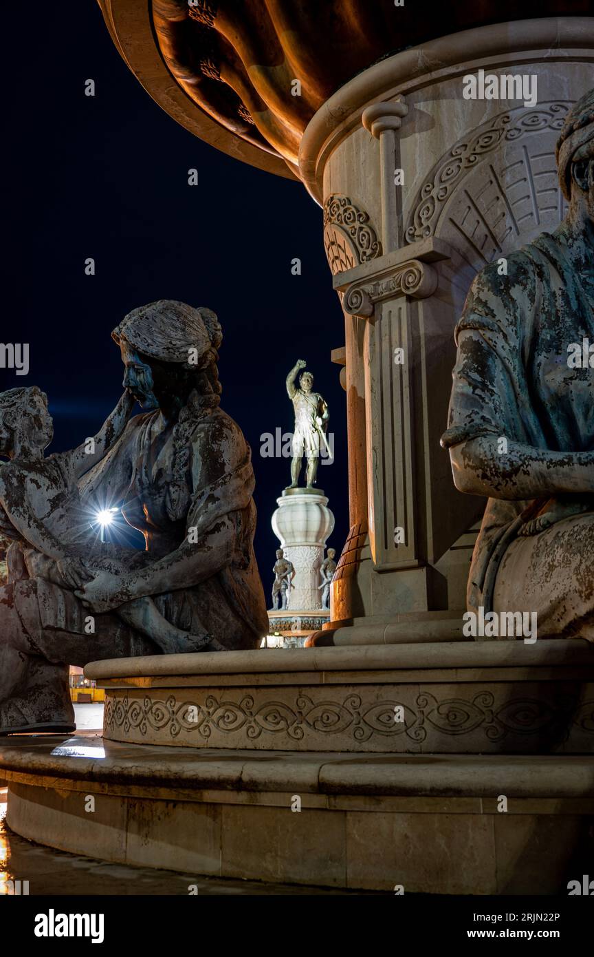 This image captures a stunning nighttime scene of the illuminated statues and clock tower of a historic fountain Stock Photo