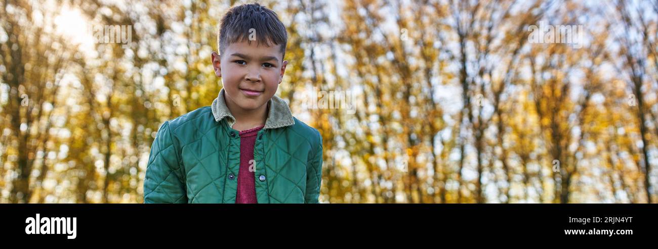 happy african american boy in outerwear looking at camera in autumn park, fall season, banner Stock Photo