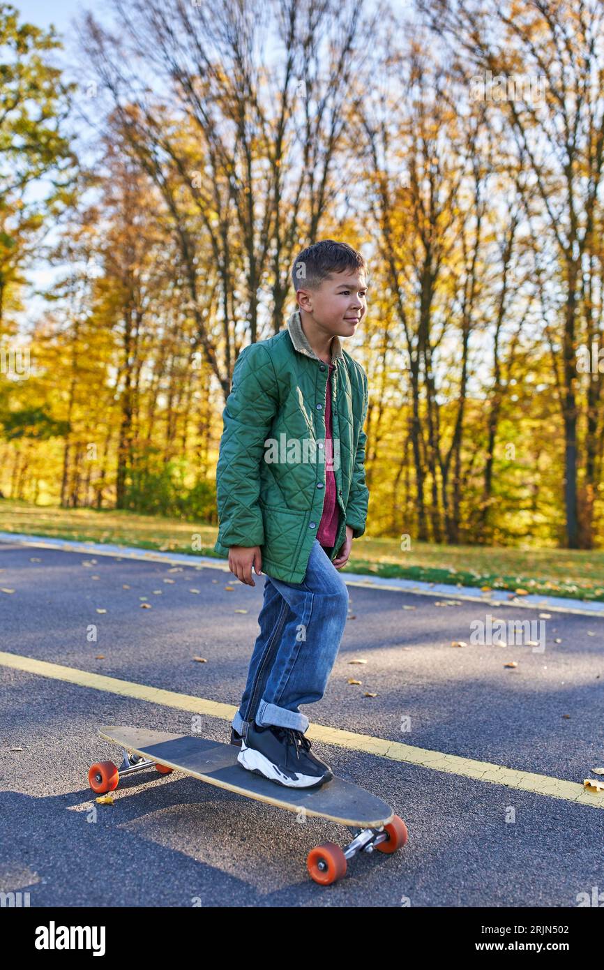 preteen african american boy in outerwear and jeans riding penny board, autumn park, fall season Stock Photo